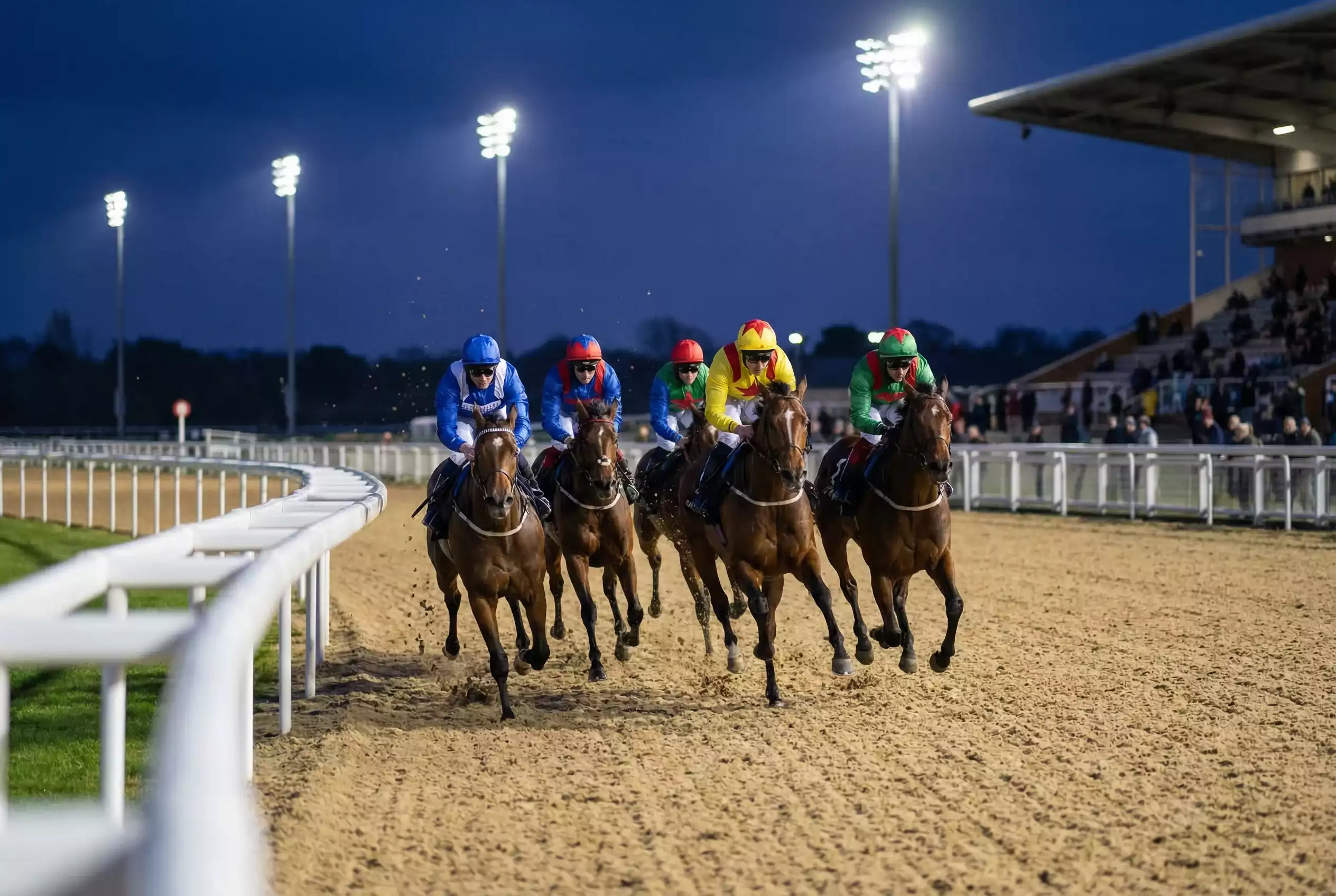Jockeys racing in a tight group on the Tapeta all-weather track at Southwell during an evening meeting under floodlights