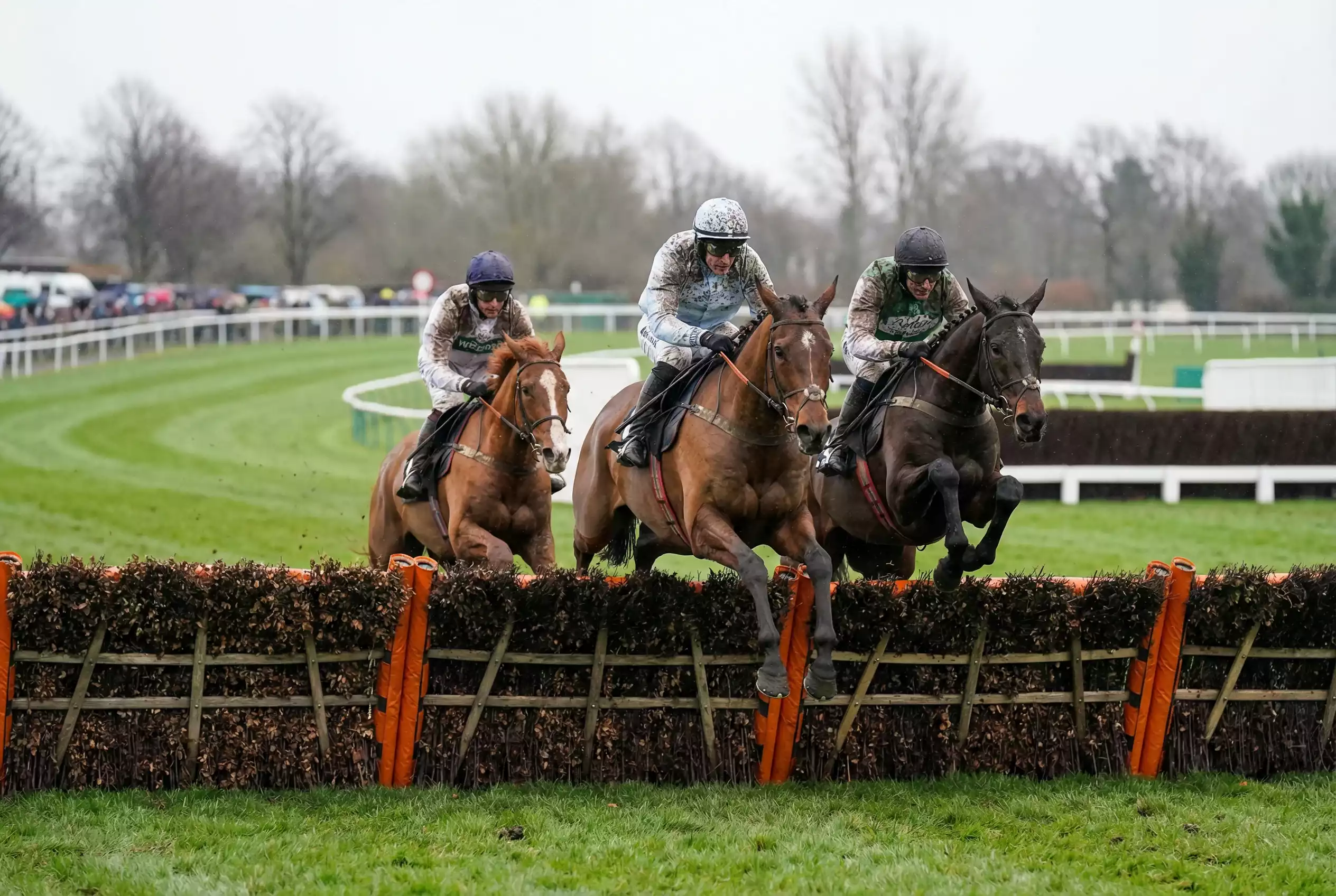 Horses clearing a hurdle on the Southwell National Hunt turf course during a jump race