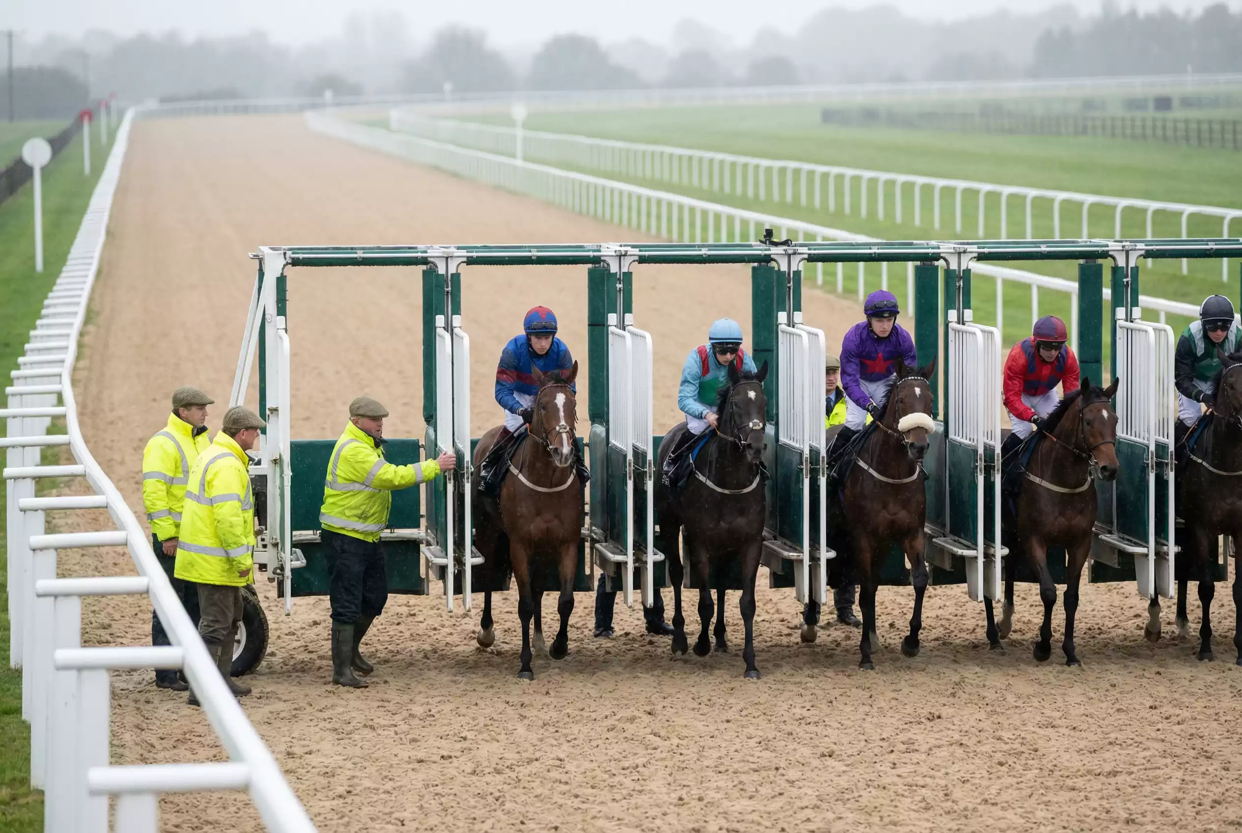 Starting stalls on the Southwell all-weather track with jockeys loading horses before a sprint race